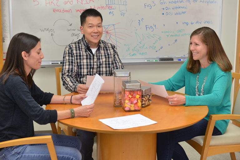 Two students and faculty member sitting at table reviewing documents