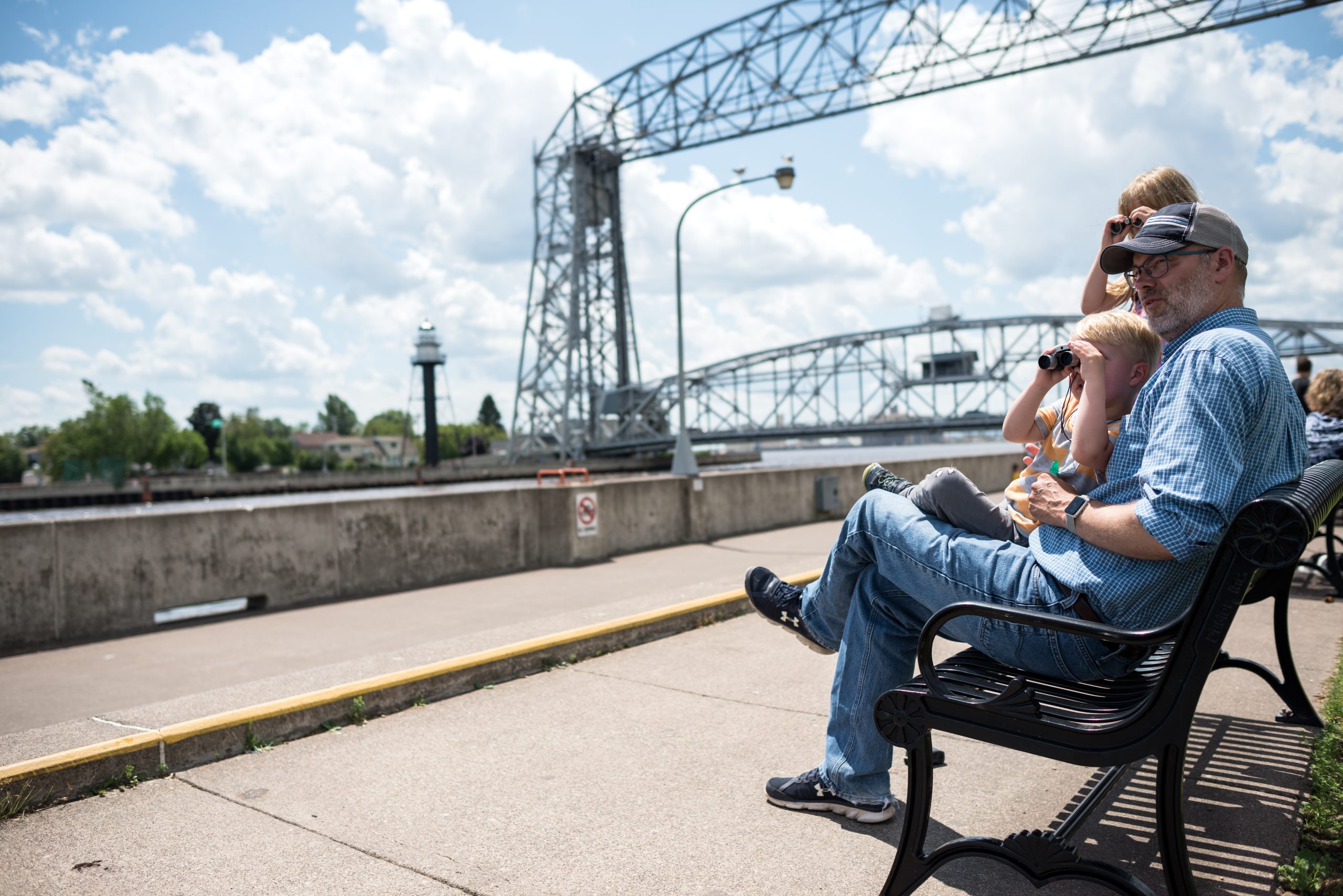 Top 5 duluth hotels for great lakes ship watching 6 A girl looks through binoculars while sitting on her grandpa's lap as her mom stands next to her with the aerial lift bridge in the background